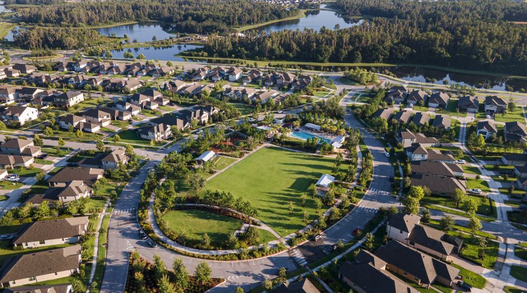 Aerial view of a Starkey Ranch neighborhood — homes around an oval park green, a community pool, roads, and lakes beyond.